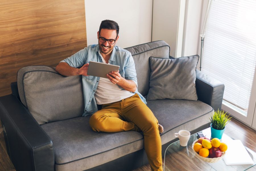 Smiling young man relaxing at home and using tablet